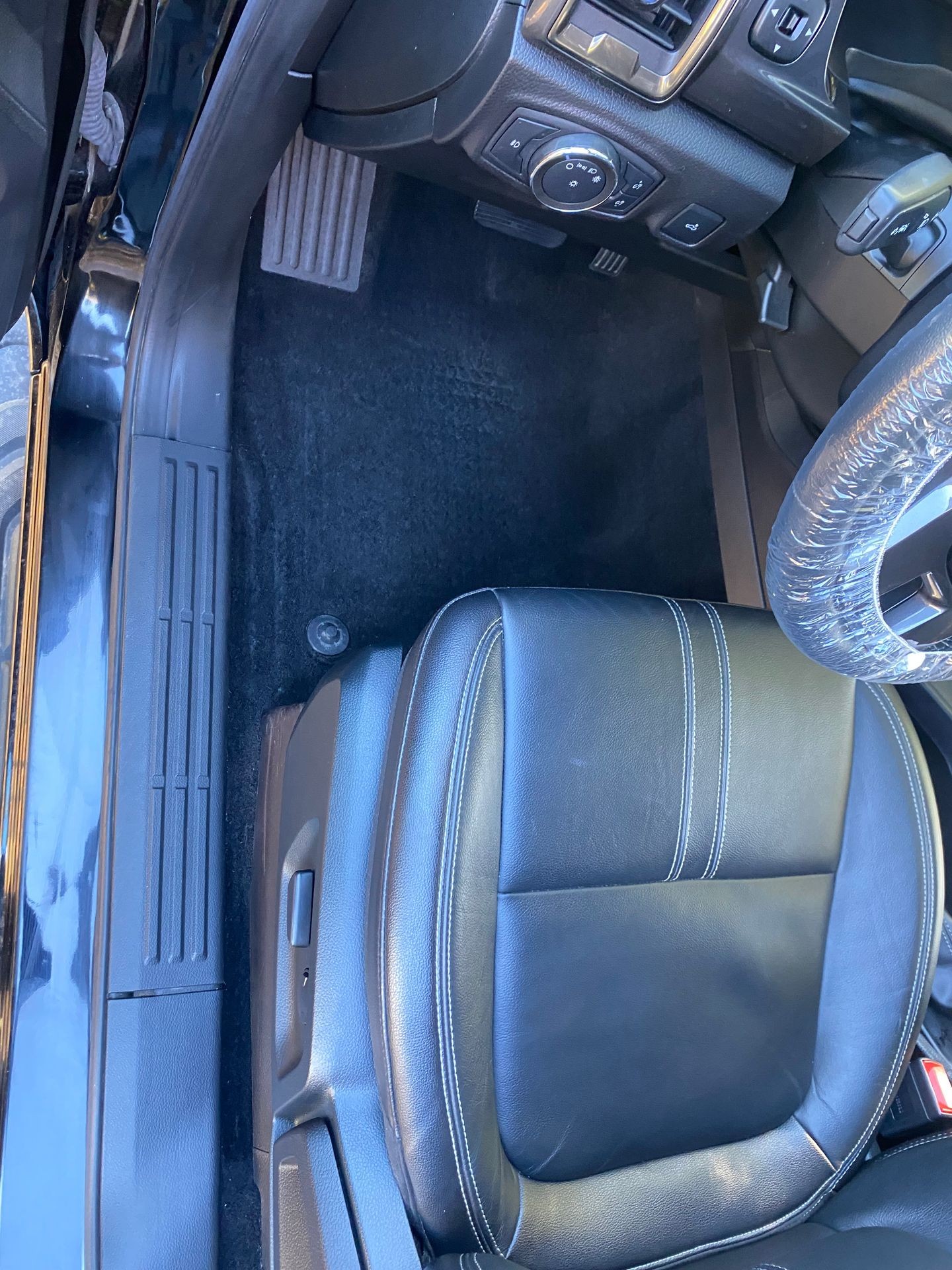 Interior view of a car showing the driver's seat, dashboard controls, and foot pedals.